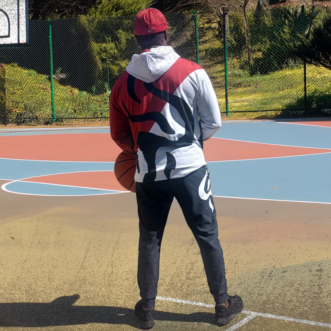 The founder of UPWEAR stands on an outdoor basketball court, holding a basketball and wearing a stylish UPWEAR hoodie and joggers featuring bold red and black flame-like designs from his own brand collection.